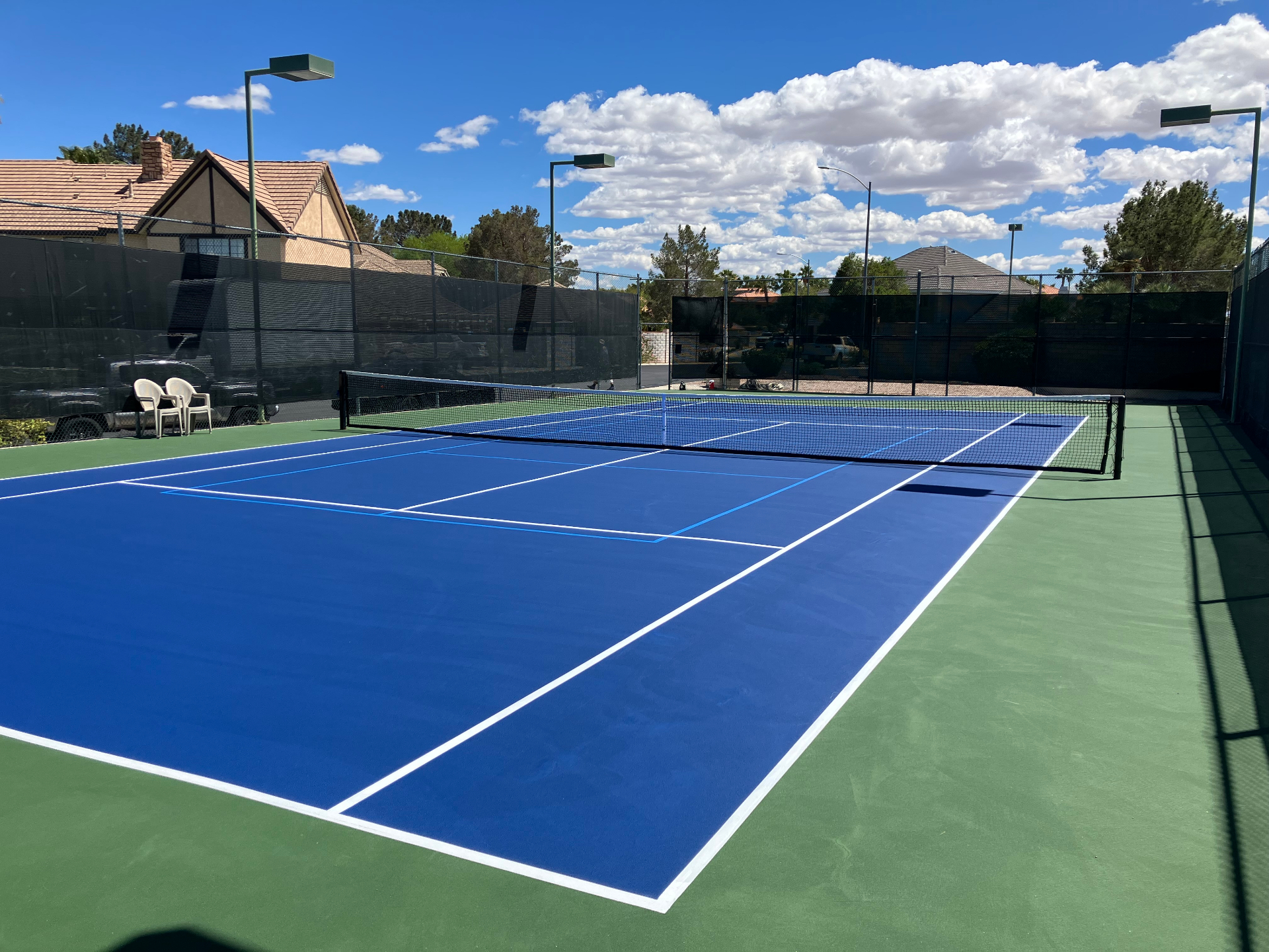 Backyard tennis court with blue playing surface and green perimeter in Southern Nevada